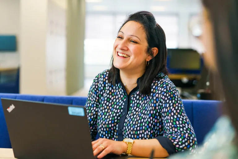 A woman smiles and looks up as she works on her laptop