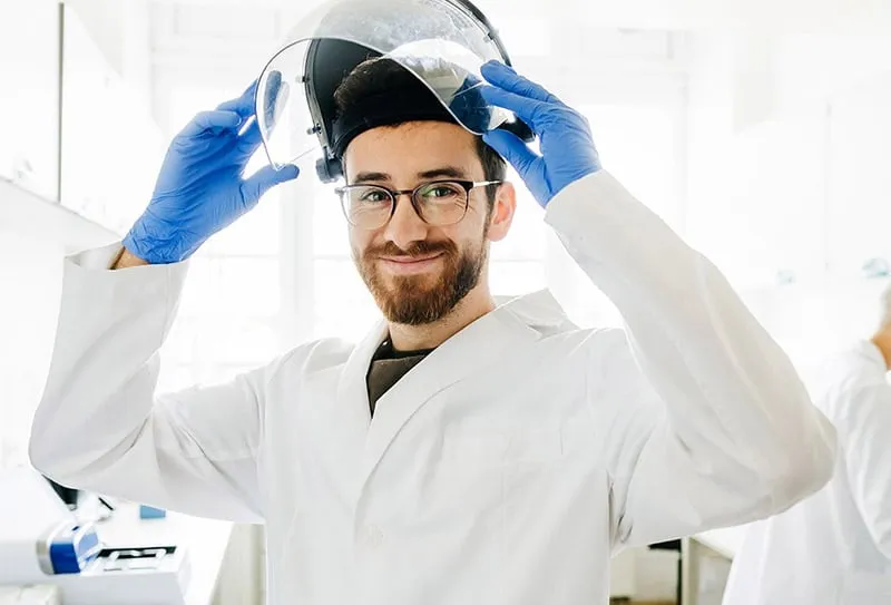 A Man in a Lab Coat Holds a Helmet, Standing in a Laboratory Setting.