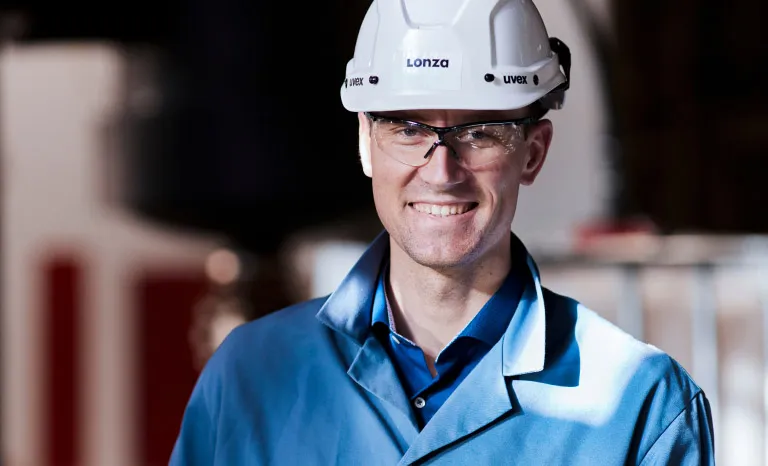 Patrick wears a construction helmet and safety gear as he smiles to camera