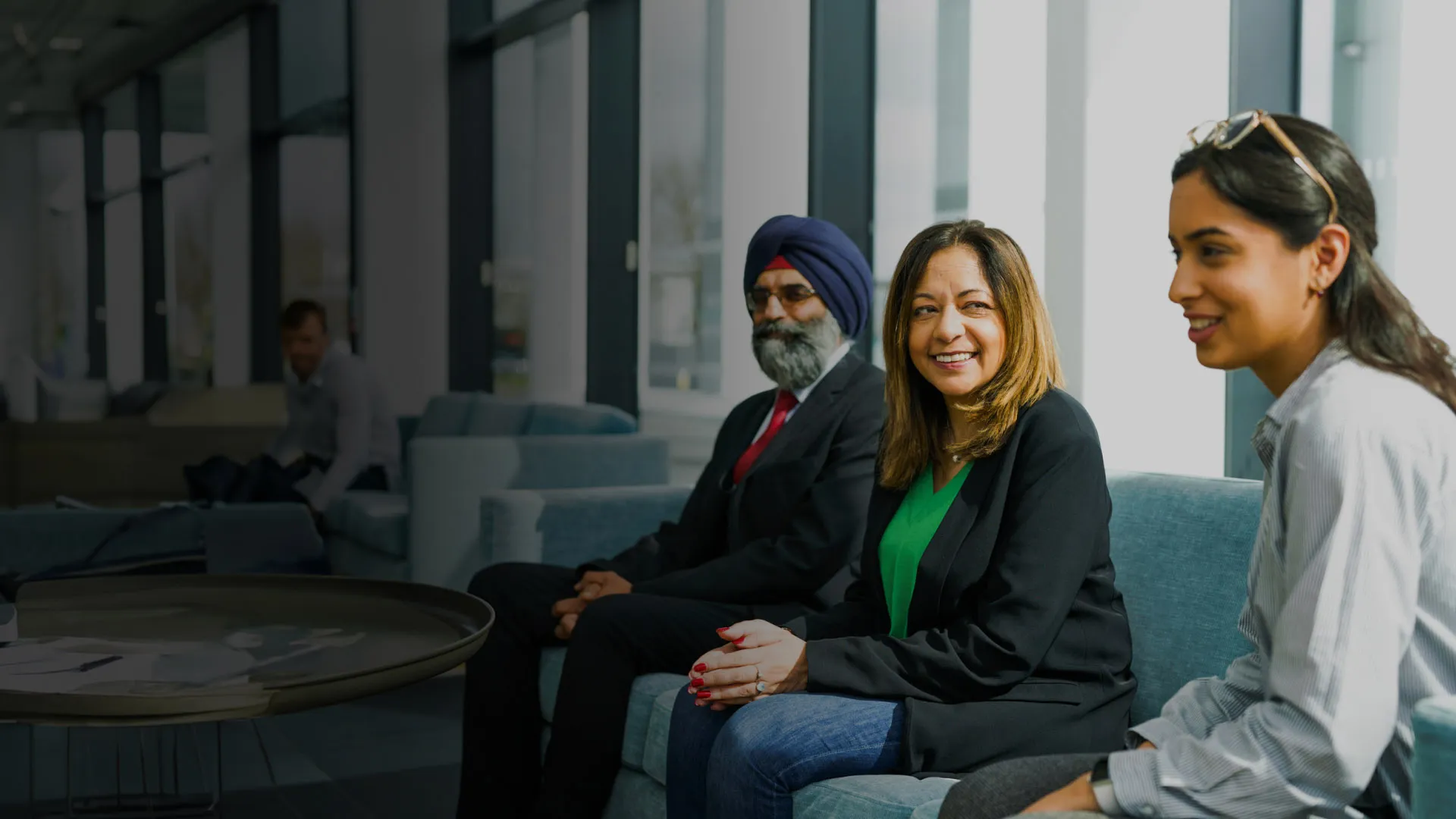 Three colleagues share a moment in a large office seating area