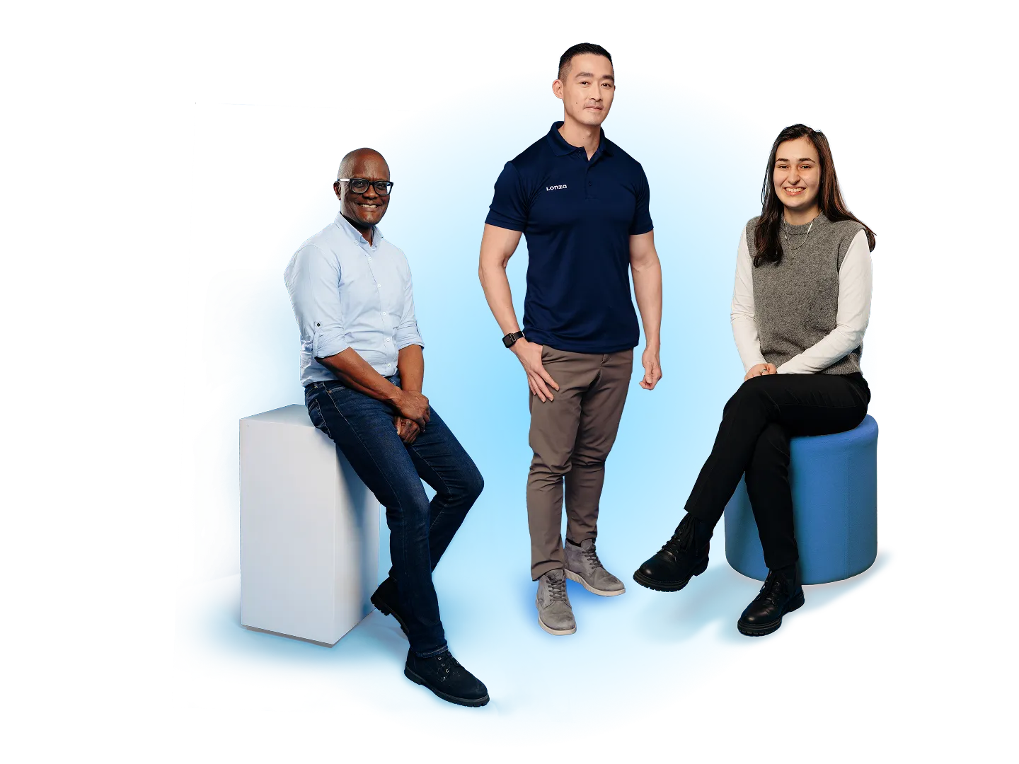 Three Professionals Posing Together Against a Solid Blue Background, With a Man Seated on a White Block, a Man Standing in the Center, and a Woman Seated on a Blue Stool..png