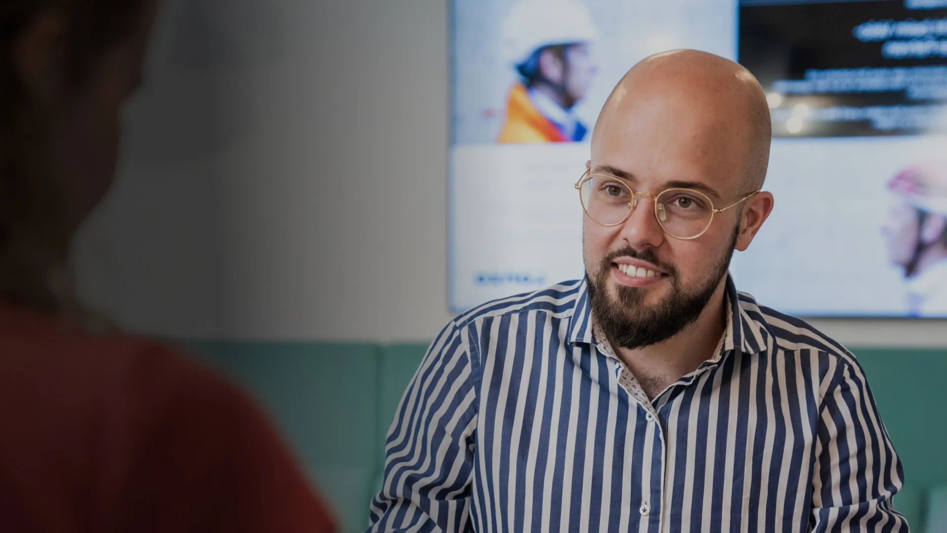 A man smiles to a colleague off camera in a meeting room setting