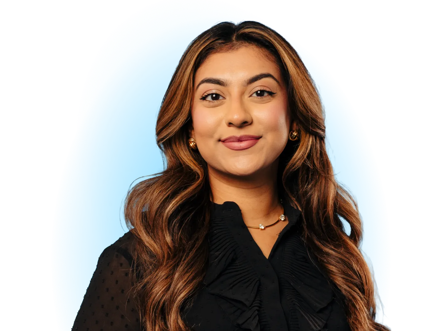 A Young Woman With Long Wavy Brown Hair Smiling Against a Solid Blue Background, Wearing a Black Ruffled Top and a Delicate Gold Necklace