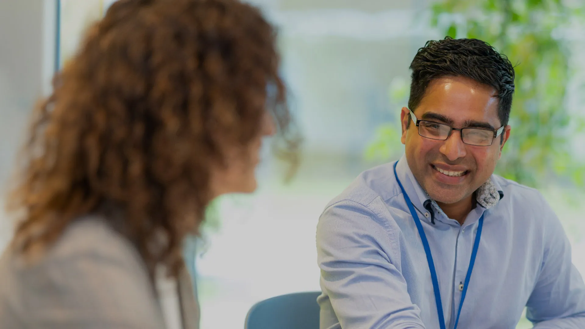 A colleague smiles to another colleague in a brightly lit meeting room