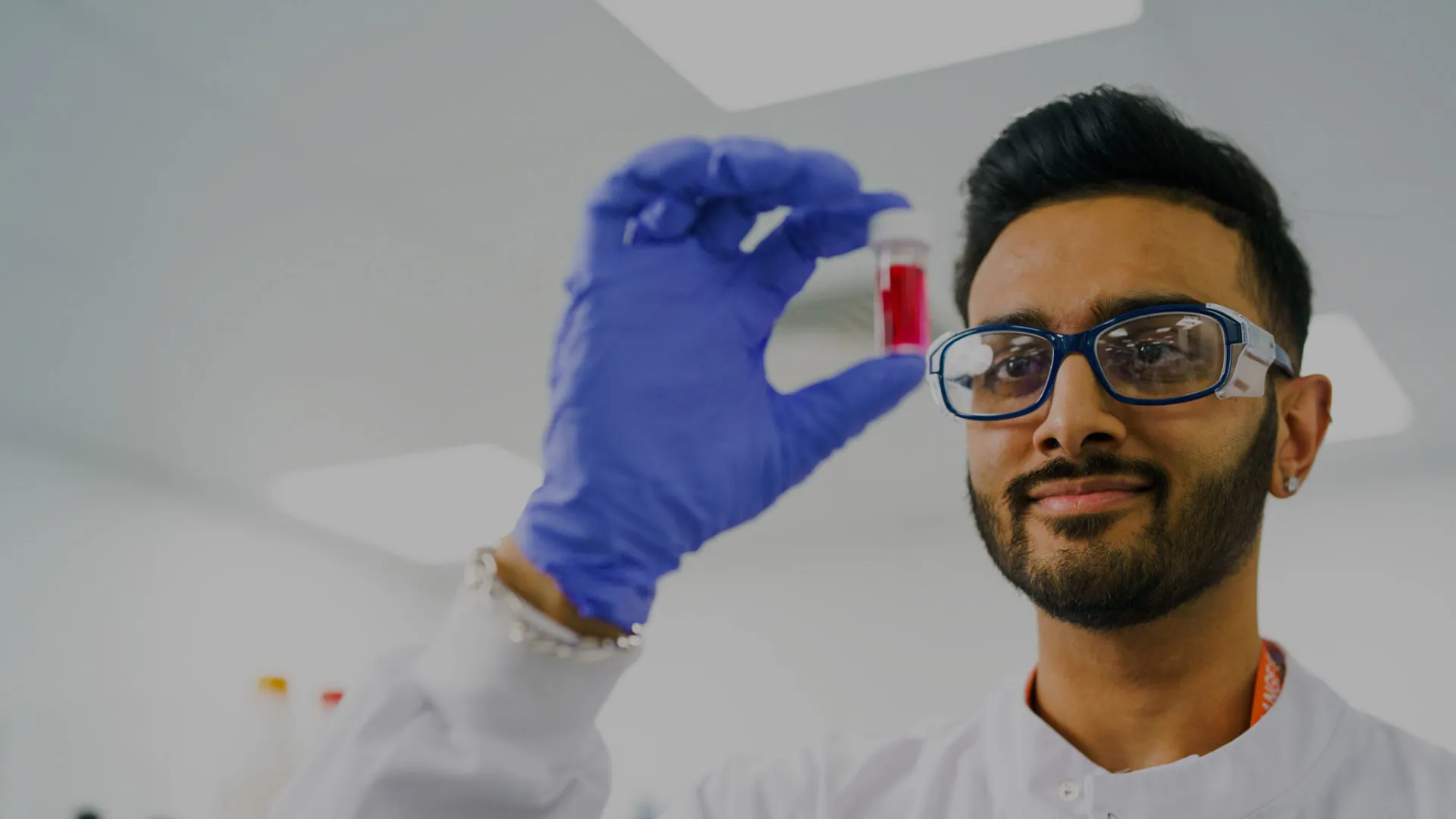 A lab worker wearing safety specs and gloves inspects a sample